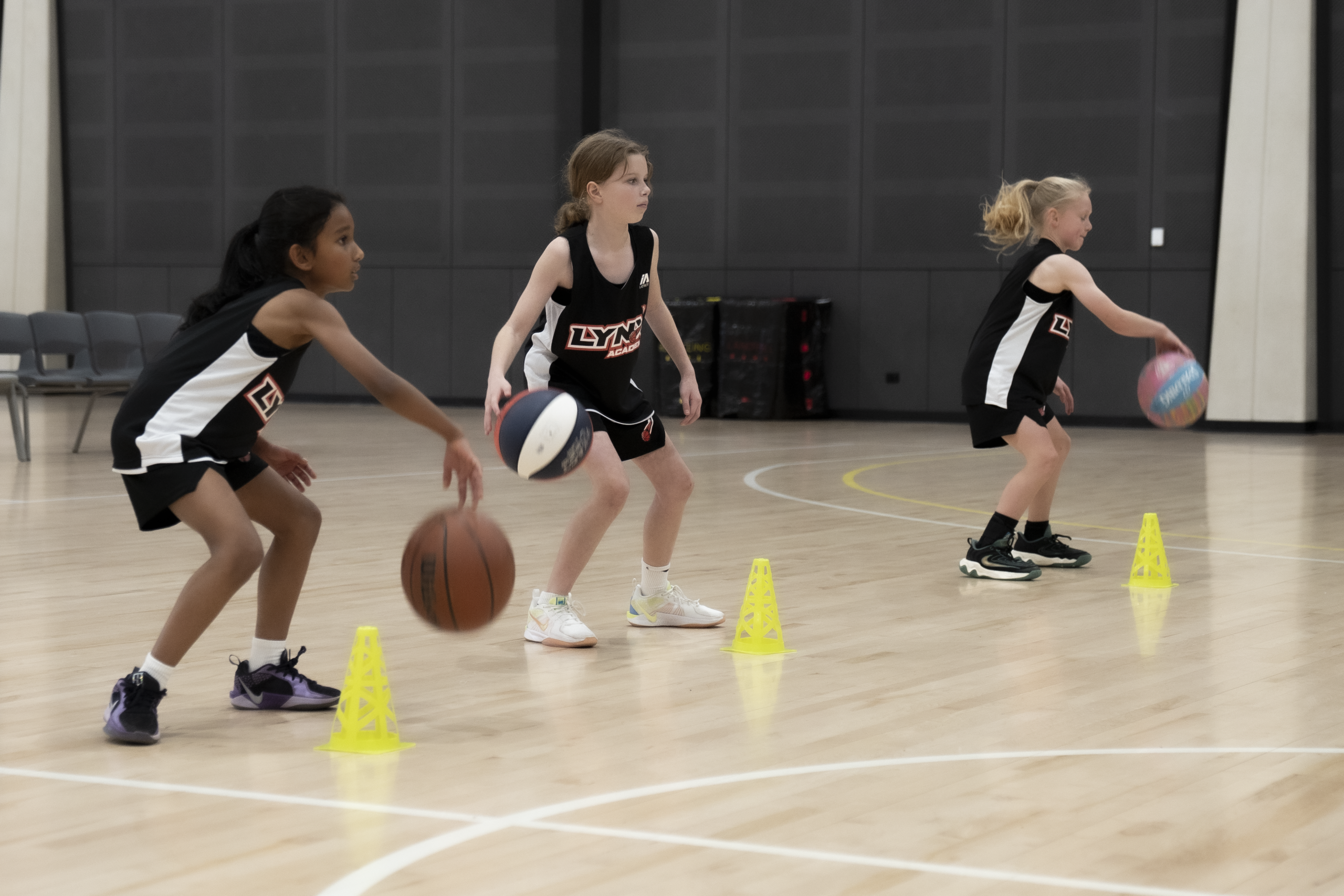 Three Lynx Academy basketball trainees navigating cone drills on indoor court as part of skill-focused coaching session