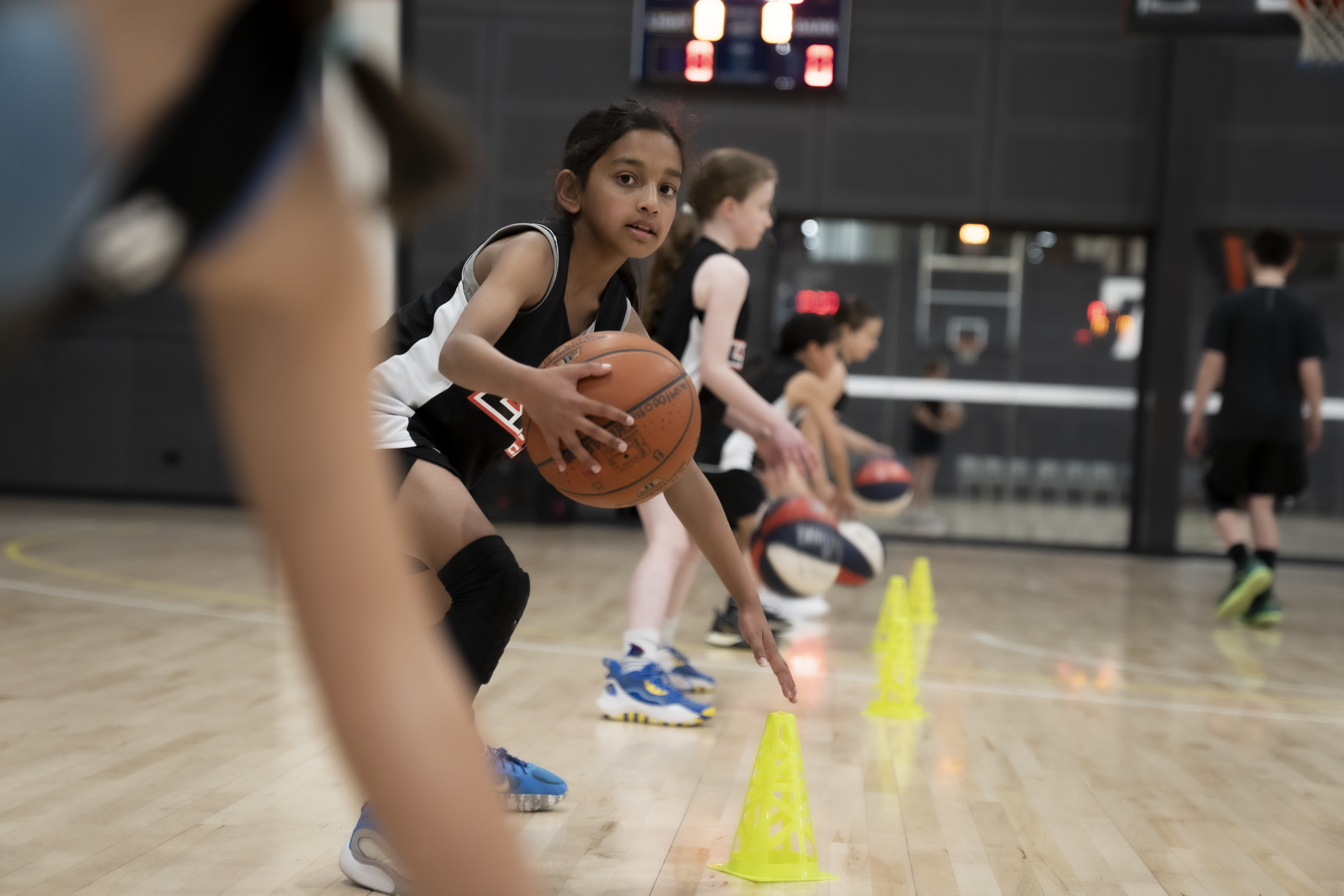 Focused Lynx Academy player leading cone dribbling drill on indoor basketball court as teammates train in background during coaching session