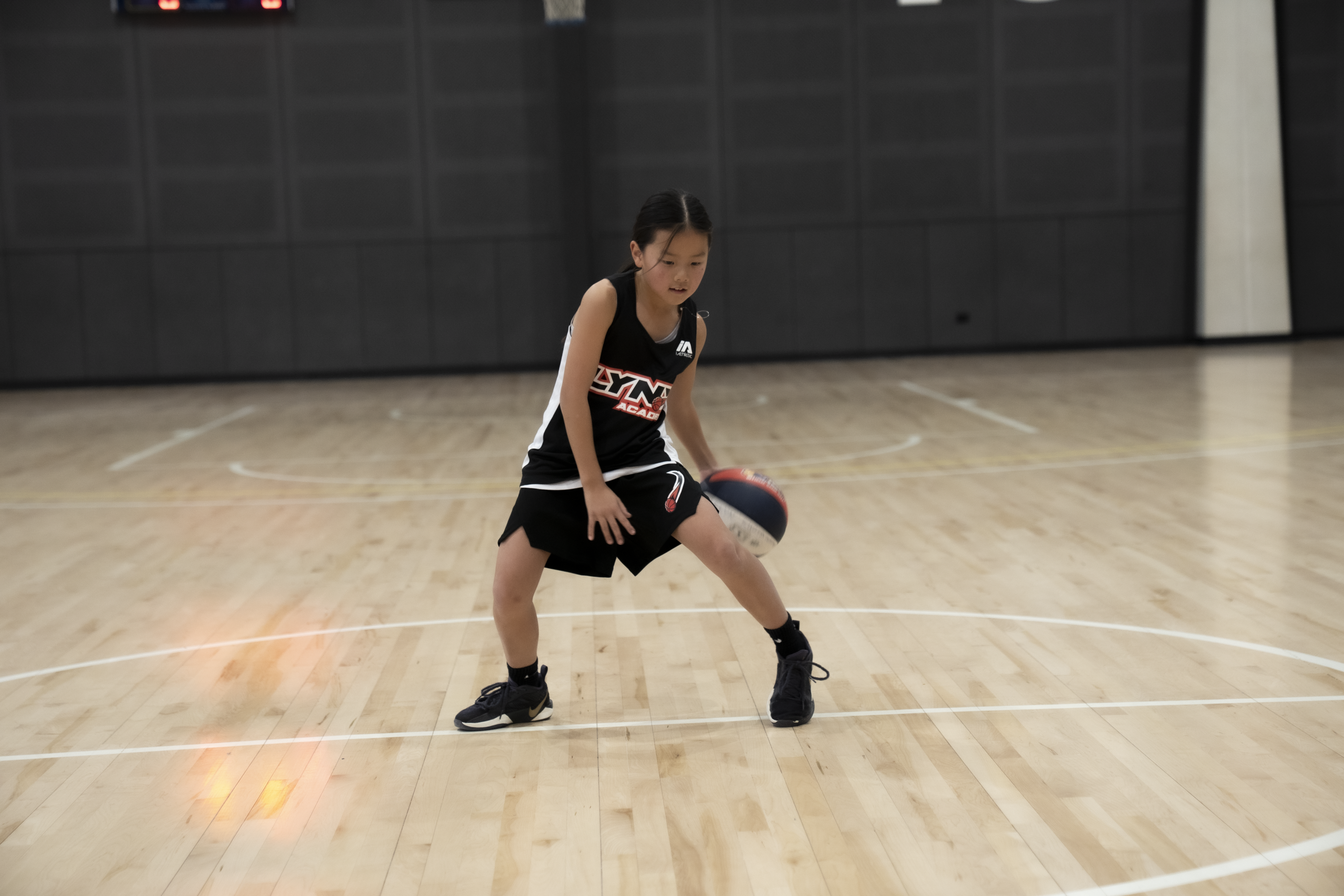 Lynx Academy student athlete in black and white jersey executing focused dribbling technique on polished indoor basketball court during coaching session